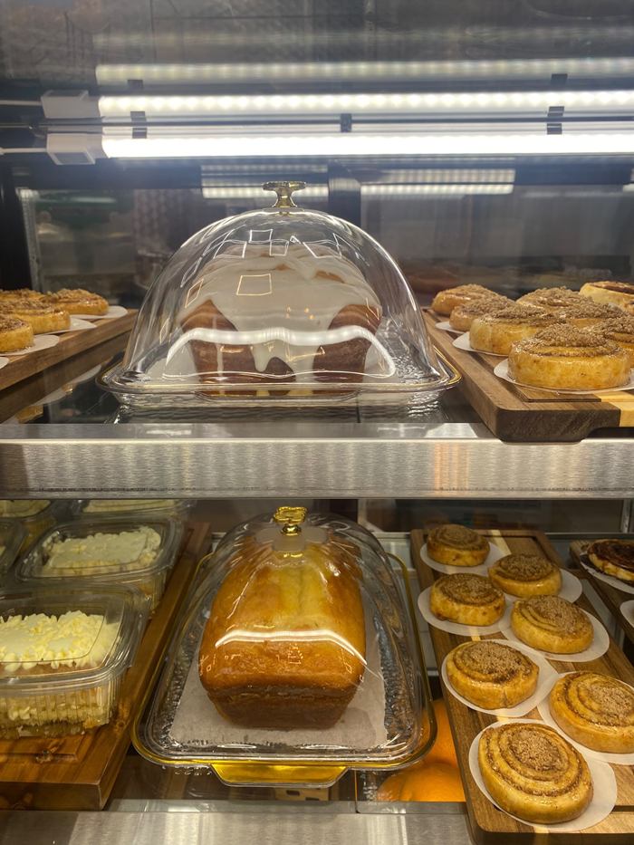 Iced loaf cake and lemon cake under glass domes, with pastries beside them