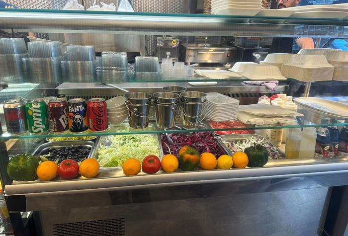 Our salad counter with shredded lettuce, red cabbage, olives, pickles and sliced onion, lined with fresh peppers, tomatoes and oranges